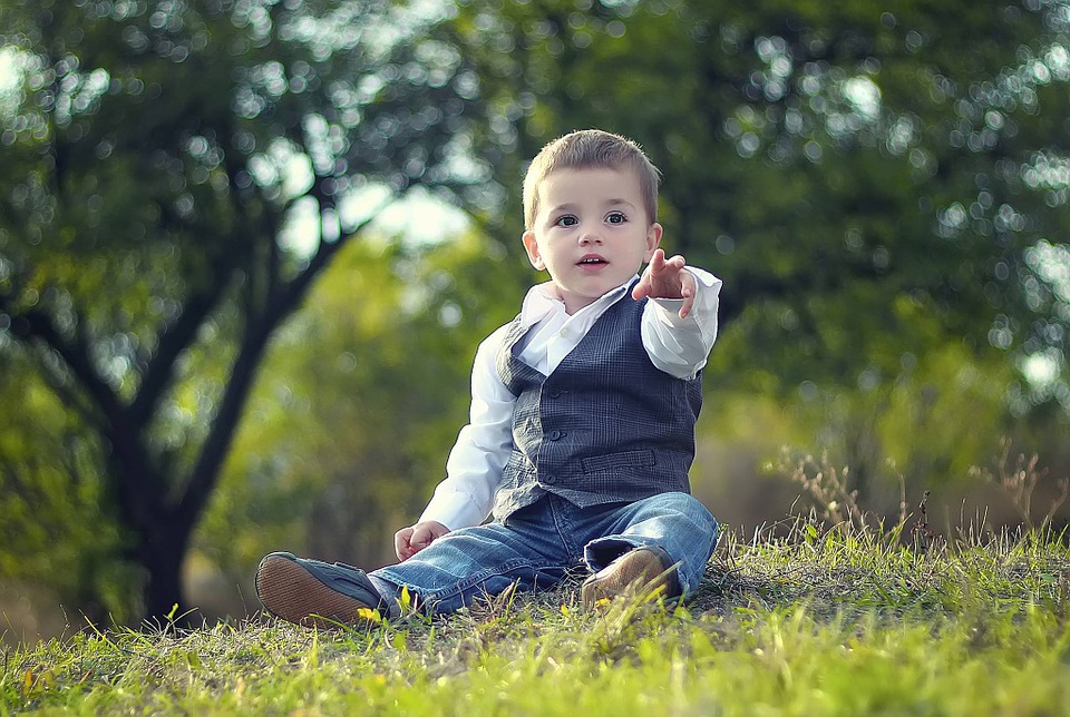 Lille dreng i børnetøj der sidder på græs, og peger